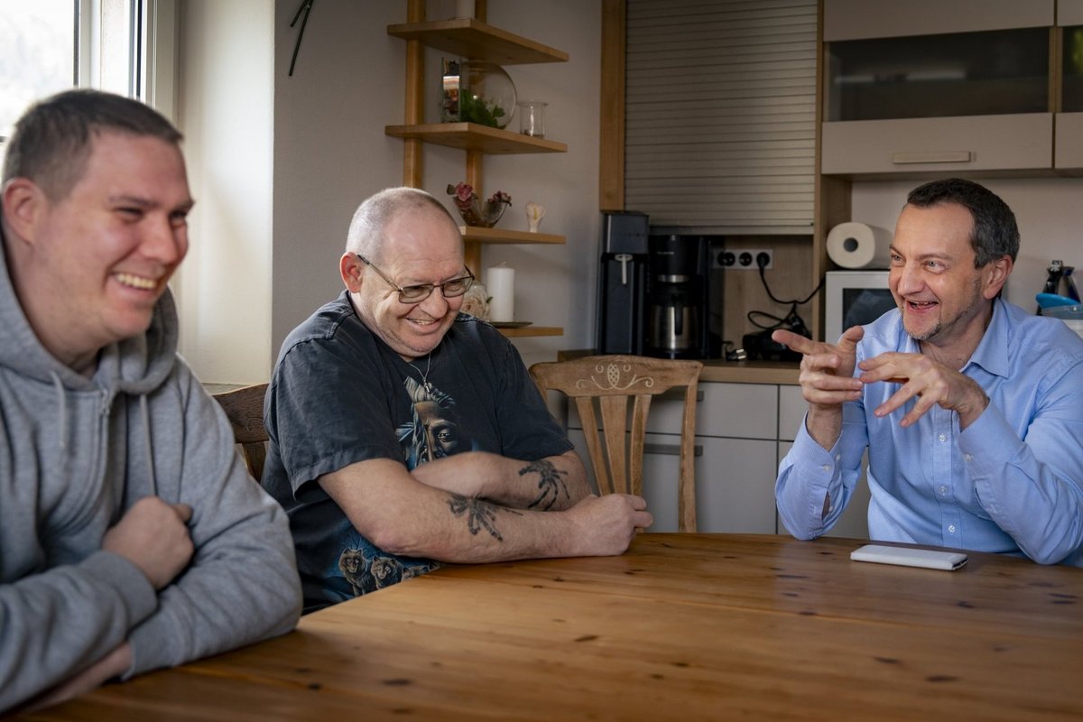 drei Maenner sitzen am Kuechentisch und unterhalten sich nett und lachen ausgelassen 